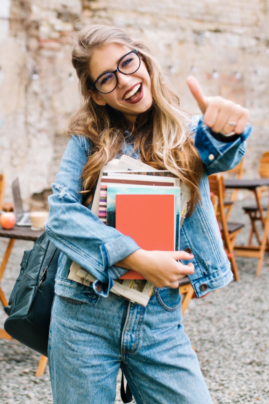 Junge Schülerin lacht und zeigt den Daumen Hoch